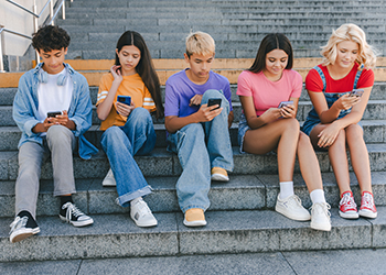 A group of teenagers on their phones sitting on school steps