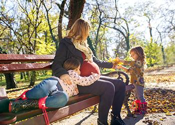 A pregnant woman plays with two children in a park