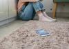 A teenage girl sits on the floor in a corner of her bedroom with a cell phone a few feet away