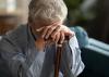 A older man leans on a walking stick with his head down